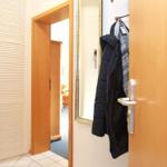 Eingangsbereich mit Kleiderhaken, Spiegel und Schrank. Tür zum Wohnzimmer sichtbar.