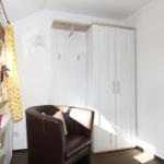 Zimmer mit braunem Sessel, weißen Schränken und Fenster mit gelben Vorhängen.
