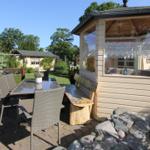 Terrasse mit Tisch, Stühlen und Holzbank neben einem Pavillon mit Glaswänden.