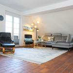Wohnzimmer mit Sofa, zwei Sesseln, Tisch und Teppich auf Terrakottboden.