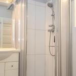 Badezimmer mit Dusche, Waschbecken und Spiegel. Weiße Fliesen und moderne Ausstattung.