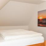 Schlafzimmer mit Dachschräge, Bett und Wandbild mit Sonnenuntergang.