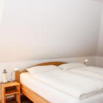 Schlafzimmer mit Doppelbett, Nachttisch und Lampe. Fenster und Heizung sind sichtbar.