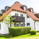 Weiße Villa mit rotem Dach und Balkon. Grün gedeckt und gepflegt.