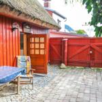 Roter Holzhaus mit Schiebetür, Tisch und Stuhl im Hof mit Steinplatten und rotem Tor.