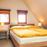Schlafzimmer mit Doppelbett, zwei Fenstern und Stehlampe.