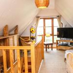 Dachgeschosszimmer mit Holzgeländer, TV und Fenster zum Garten.