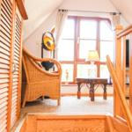 Durchgang in ein Zimmer mit Holzgeländer, Wickerstuhl und Fenster.