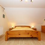 Schlafzimmer mit Holzbett, Nachttischen und Schrank. Fenster mit Blick auf Wald.