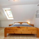 Schlafzimmer mit Holzbett, Dachfenster und weißen Wänden.