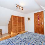 Schlafzimmer mit Holzbett, Kleiderschrank und Wickerstuhl unter Dachschrägen.