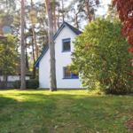 Ein weißes Haus mit blauen Fensterrahmen steht in einem grünen Garten mit Bäumen und Sträuchern.