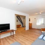 Wohnzimmer mit Sofa, Fernseher und Holzboden. Treppe führt in den zweiten Stock.
