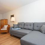 Wohnzimmer mit grauem Sofa, Holzboden und Wicker-Sessel.