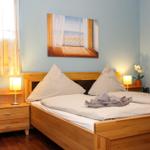 Schlafzimmer mit Holzbett, Nachttisch und Wandbild. Fenster mit Vorhängen.