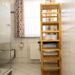 Badezimmer mit Dusche, Toilette und hölzernem Regal.