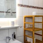 Badezimmer mit Waschbecken, Spiegel und Holzregal. Fliesenwand mit dekorativer Bordüre.