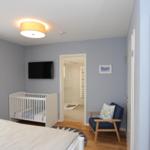 Schlafzimmer mit Babybett, Fernseher und Blick in die Dusche.