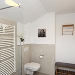 Badezimmer mit Dusche, Toilette, Heizung und Holzregal an der Wand.