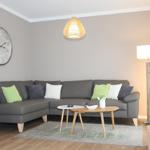 Wohnzimmer mit grauem Sofa, Holztisch und Wanduhr.