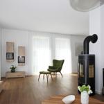 Wohnzimmer mit Holzboden, grüner Sessel, Kaminofen und großem Fenster