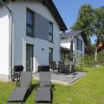 Moderne Villa mit Terrasse, Gartenmöbeln und Grillplatz. Grünflächen und Bäume umgeben das Haus.