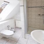Badezimmer mit Dusche, Toilette und Waschbecken unter Dachschräge mit Fenster.