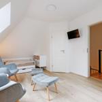 Schlafzimmer mit Dachschrägen, Bett, zwei Sesseln und Fernseher an der Wand.