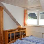 Schlafzimmer mit Babybett, Bett und Holzschrank unter Dachschräge mit Fenster.