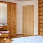 Schlafzimmer mit Holzmöbeln, Bett und Kleiderschrank. Tür und Leiter sichtbar.