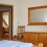 Schlafzimmer mit Holzmöbeln und Spiegel. Durchgang zu einem weiteren Raum mit Bett.