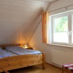Schlafzimmer mit Holzbett, Fenster und Stuhl.