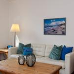 Wohnzimmer mit Sofa, Holztisch und Wandbild. Fenster mit Blick nach draußen.