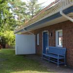Ein Haus mit Backsteinfassade, blauer Tür und Bank. Hinterhof mit Garten und Holzgarage.