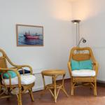 Zwei Rattan-Stühle mit Kissen, kleiner Tisch und Wandbild mit Boot.