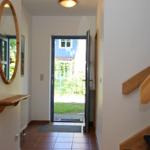 Eingangsbereich mit Holztreppe, Spiegel und offener Tür zum Garten.