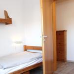 Schlafzimmer mit Holzbett, Wandregal und Tür zum Ankleidebereich.
