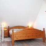 Schlafzimmer mit Holzbett, Kleiderschrank und Nachttisch unter schrägen Wänden.