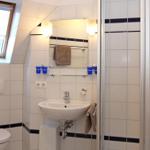 Badezimmer mit Dusche, Waschbecken und Toilette. Weiße Fliesen mit dunklen Streifen.