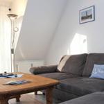 Ein Wohnzimmer mit grauem Sofa, Holztisch und Fenster mit weißen Vorhängen.