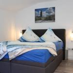Schlafzimmer mit Bett, Wandbild und Nachttisch. Fenster mit Vorhängen.