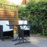 Terrasse mit zwei Stühlen und Tisch, umgeben von Hecke und Holzzaun.
