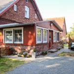 Rotes Holzhaus mit Garten und Terrasse. Eingangstür und Fenster mit weißen Rahmen.