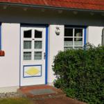 Eingangstür mit gelbem Sonnenmotiv, weiße Wände, blaue Fensterrahmen und roter Ziegeldach