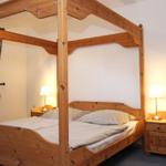 Schlafzimmer mit Holzbett, Nachttischen und Stuhl. Fenster mit Vorhängen.
