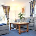 Wohnzimmer mit grauem Sofa, Holztisch und blauen Gardinen.