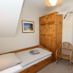 Ein Schlafzimmer mit Holzbett, Kleiderschrank und Stuhl. An der Wand hängt ein Bild.