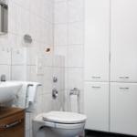 Badezimmer mit Waschbecken, Toilette und Dusche. Weiße Fliesen und Schränke.