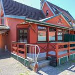 Rotes Ferienhaus mit Terrasse und Holzgeländer. Eingangstür und Fenster sind sichtbar.