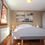Schlafzimmer mit weißem Bett, grauer Sitzbank, Wandbildern und Fenster mit Jalousie.